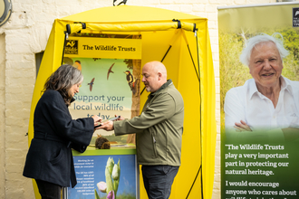 a membership recruiter talking to a member of the public with a membership stall in the background with a wildlife trust sign above.