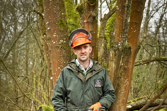 Adam stands with a chainsaw in a wood