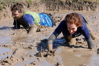 Two people laughing whilst crawling through mud