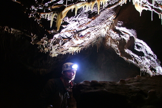 man with head torch deep underground beneath stalactites