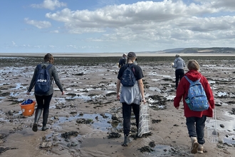 A group of people walking along the sea shore with survey equipment