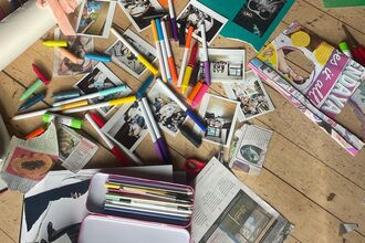 messy scattered pens, polaroid photos, coloured card and people's feet in shoes on wooden floorboards
