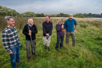 Group of people outdoors holding shovels and rakes, smiling.