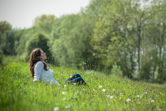 Young woman enjoys being outside in the sun, sat in a meadow