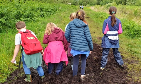 Children dressed in their outdoor gear and wellies standing in thick mud on Westhay Nature Reserve