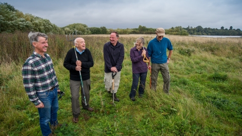 Group of people outdoors holding shovels and rakes, smiling.