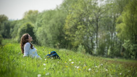 Young woman enjoys being outside in the sun, sat in a meadow