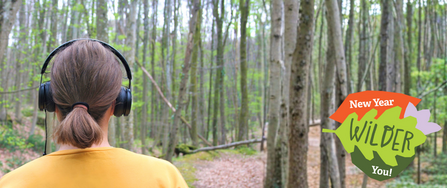 A woman with headphones on, standing in a woodland
