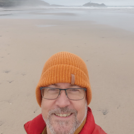 Ian Egerton on a beach wearing a mustard yellow beanie hat