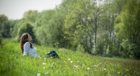 Young woman enjoys being outside in the sun, sat in a meadow