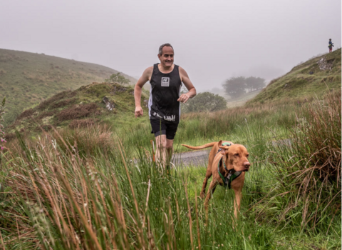 Steve running alongside a dog at a misty Man vs Moor