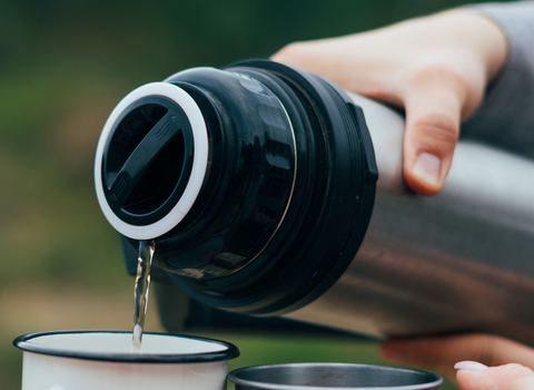 A hand pouring tea into two cups outdoors from a flask