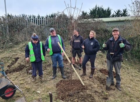 a group of people smile next to a tree they have planted