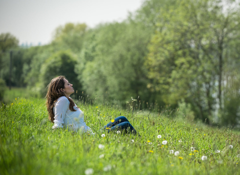 Young woman enjoys being outside in the sun, sat in a meadow